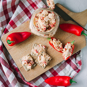 An overhead picture of a jar filled with pimento cheese, crackers, and mini red peppers on a cutting board.