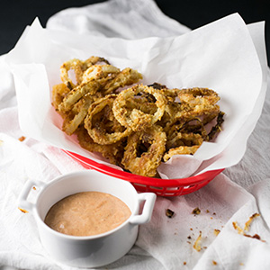 Coated with a combination of cracker and potato chip crumbs and served with a spicy, creamy sauce, these oven-fried onion rings are a perfect side or snack! | Recipe from Chattavore.com